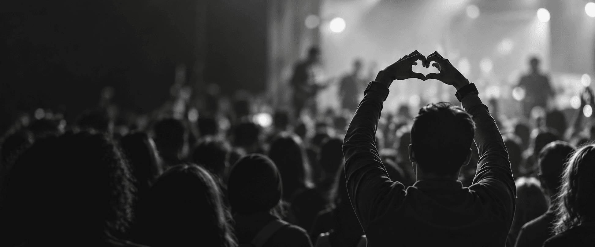 A person makes a heart shape with their hands in a crowd